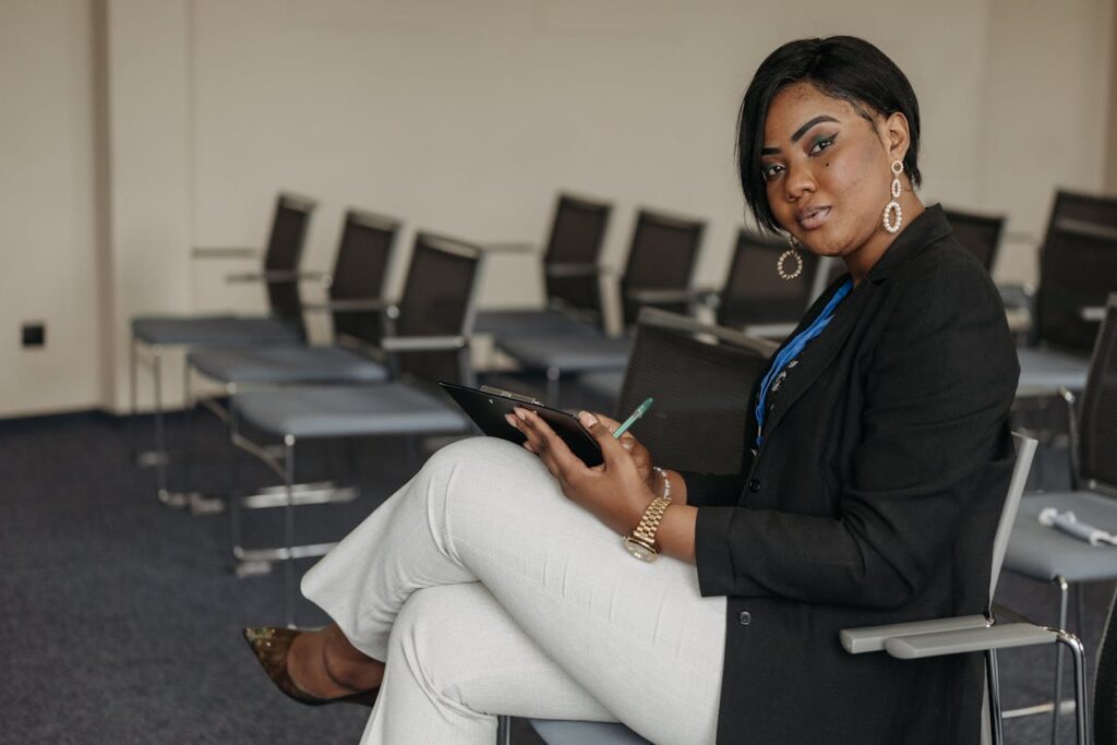 African American woman in business attire sitting in a meeting room holding a clipboard.