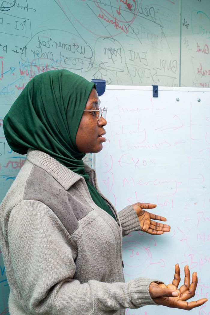 Female teacher in hijab explaining lesson with gestures at whiteboard in a classroom setting.